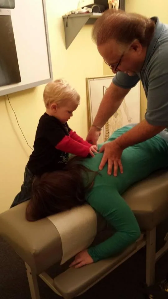 Adult chiropractor examining small child sitting on treatment table in clinical setting