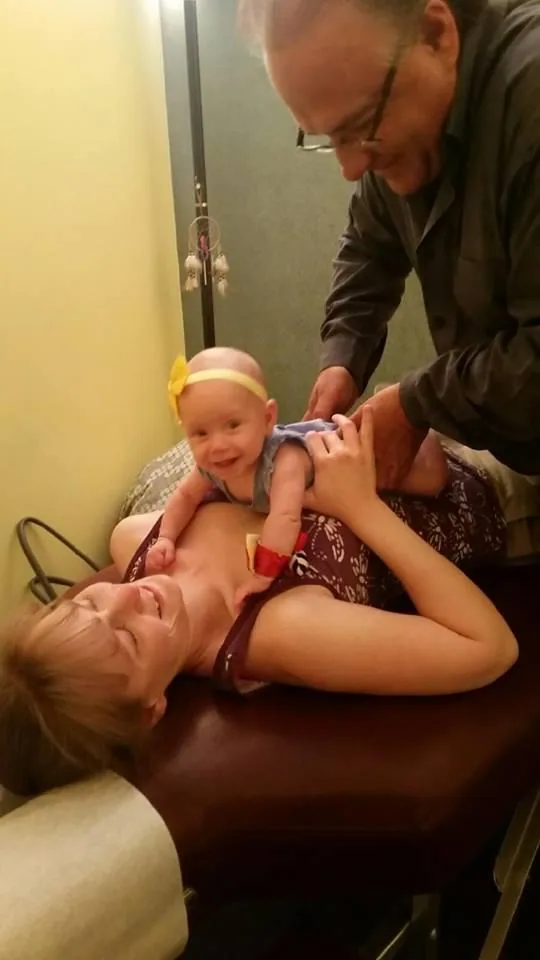 Chiropractor examining infant while parent holds baby on examination table