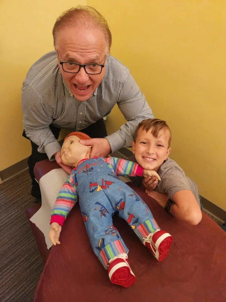 Adult man and young child posing together with a doll against yellow wall