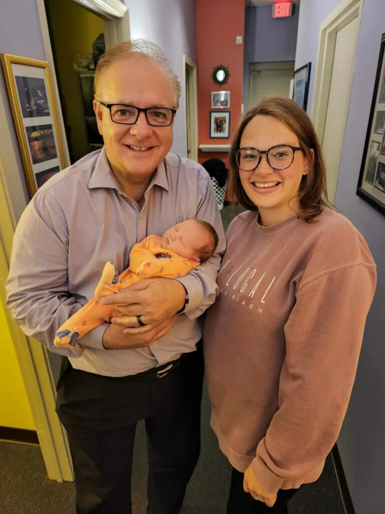 Man and woman holding infant in yellow blanket inside office hallway